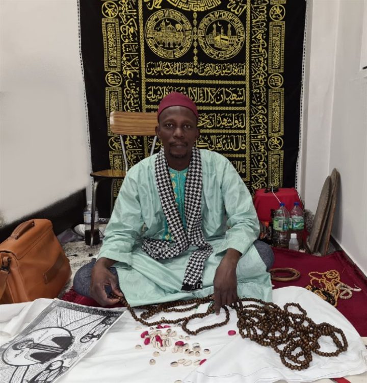 Master Bodou, seated with his prayer beads and cowrie shells